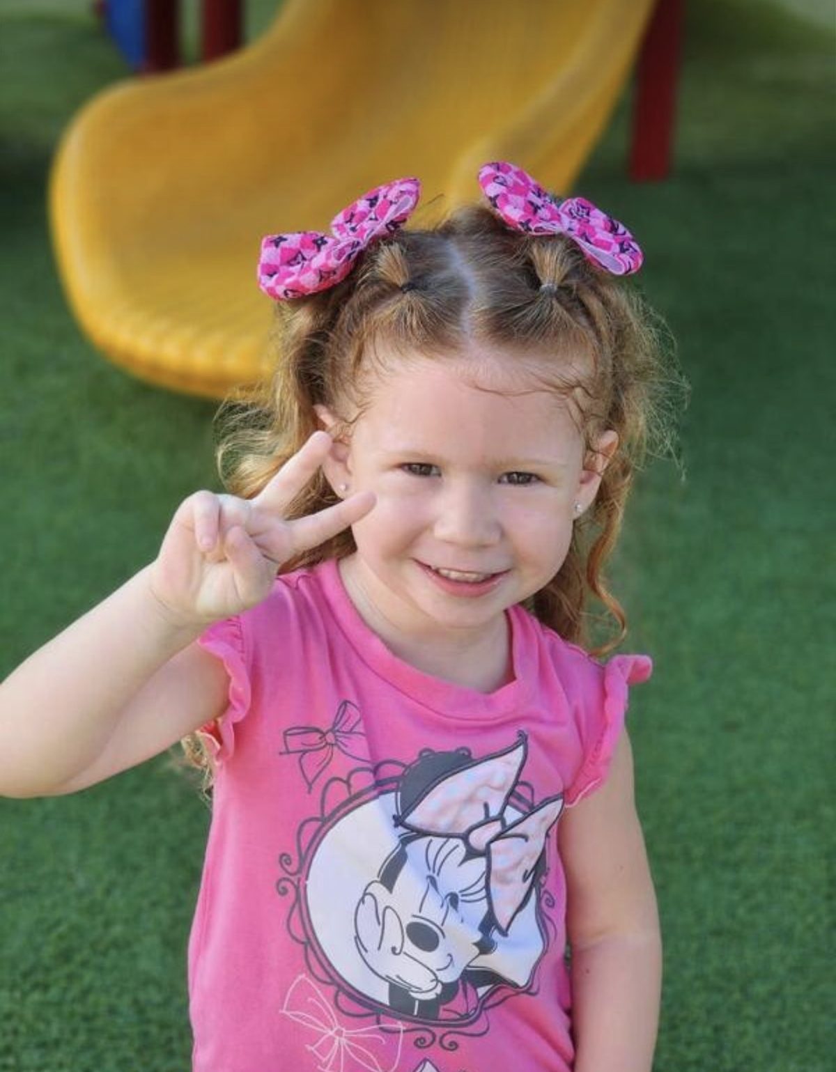 A preschooler flashing a peace sign on the playground